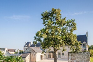 Ein Steingebäude mit einem großen Baum davor, umgeben von weiteren Steinhäusern.