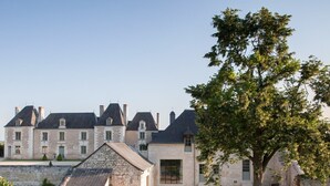 Un grand bâtiment en pierre, doté de nombreuses cheminées, avec un arbre imposant en premier plan.