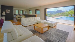 Ein modernes Wohnzimmer mit einer großen Eckcouch, einem Couchtisch und Blick auf einen Swimmingpool und Berge.