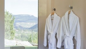 Ein Badezimmer mit zwei weißen Bademänteln, die an einer Wand hängen, und einer Glastür, die auf einen Balkon mit Bergblick führt.