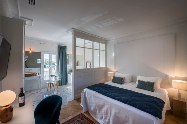 Une chambre d’hôtel comprenant un lit, une table de chevet, une lampe et donnant sur la salle de bain et l’espace repas.