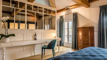 Une chambre avec une grande fenêtre, une armoire en bois, un bureau avec une chaise et un lit recouvert d’une couverture bleue.
