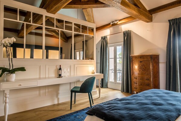 Une chambre avec une grande fenêtre, une armoire en bois, un bureau avec une chaise et un lit recouvert d’une couverture bleue.