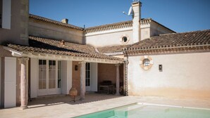 A pool area with a tiled deck, a covered seating area, and a building with a tiled roof and columns. - Chateau Grand Cru - Five Bedroom Castle, Sleeps 10 (Saint-Emilion)