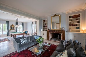 A spacious living room with a pool table, sofas, a fireplace, and a bookshelf.