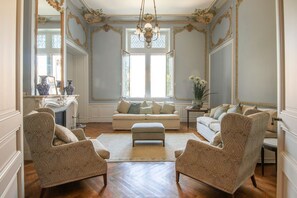 A spacious living room with a large window, ornate ceiling, and classic furniture.