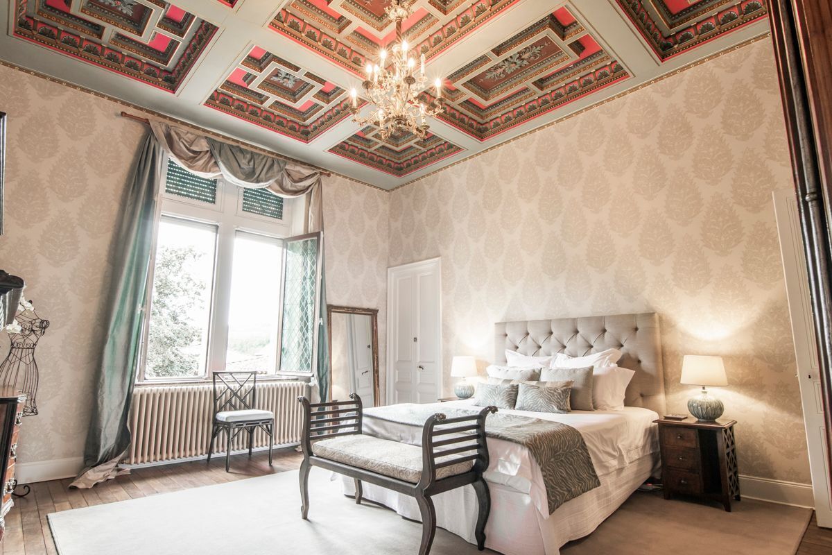 Een slaapkamer met een groot bed, een kroonluchter en een raam met gordijnen.