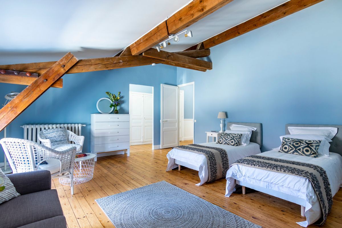 Une chambre avec deux lits, une commode, une chaise et un radiateur.