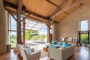 A spacious living area with wooden beams, large windows, and a view of the outdoors. - Maison Des Pivoines - Six Bedroom Villa, Sleeps 10 (Verteillac)