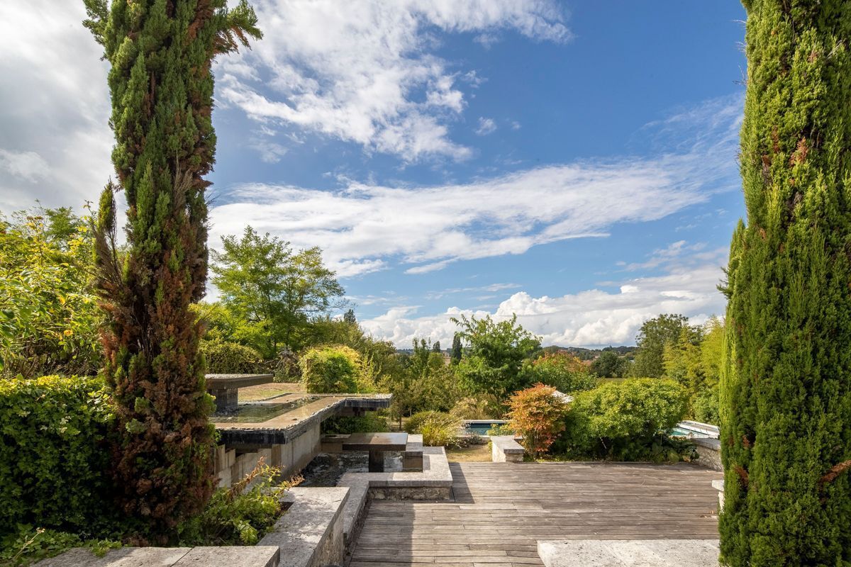 Une terrasse en bois avec des marches en pierre menant à un espace de détente entouré d’une végétation luxuriante et de grands arbres.