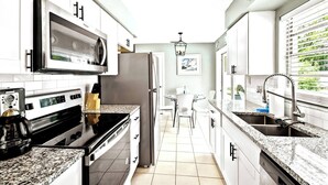Una cocina moderna con armarios blancos, electrodomésticos de acero inoxidable, encimeras de granito y vistas a zonas verdes por la ventana.
