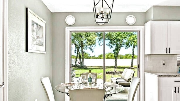 Comedor con mesa y sillas de vidrio, una lámpara colgante y vistas al exterior.
