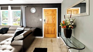 Una sala de estar con un sofá, una puerta de madera, un reloj de pared y una planta en maceta.