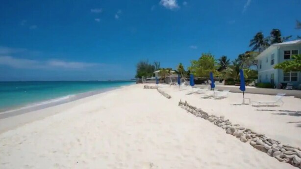 Ein Strand mit weißem Sand, klarem, blauem Wasser und einem Gebäude mit hellblauer Fassade.