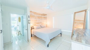 Ein Schlafzimmer mit einem Bett, einer Holzwand, einem Deckenventilator und Blick ins Freie.
