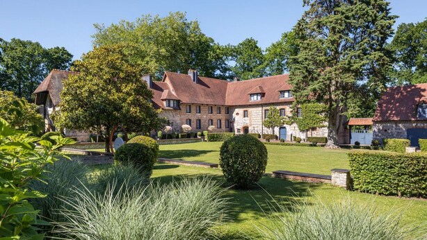 A historic building with a courtyard, stone walls, and mature trees.