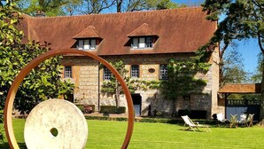 A stone building with a red roof, a lawn with chairs, and a large circular sculpture.