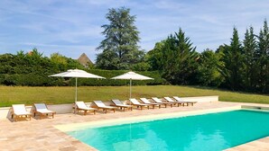 A swimming pool with lounge chairs and umbrellas, surrounded by greenery and a pyramid structure in the background. - Chartreuse Des Roses (Pinsac)