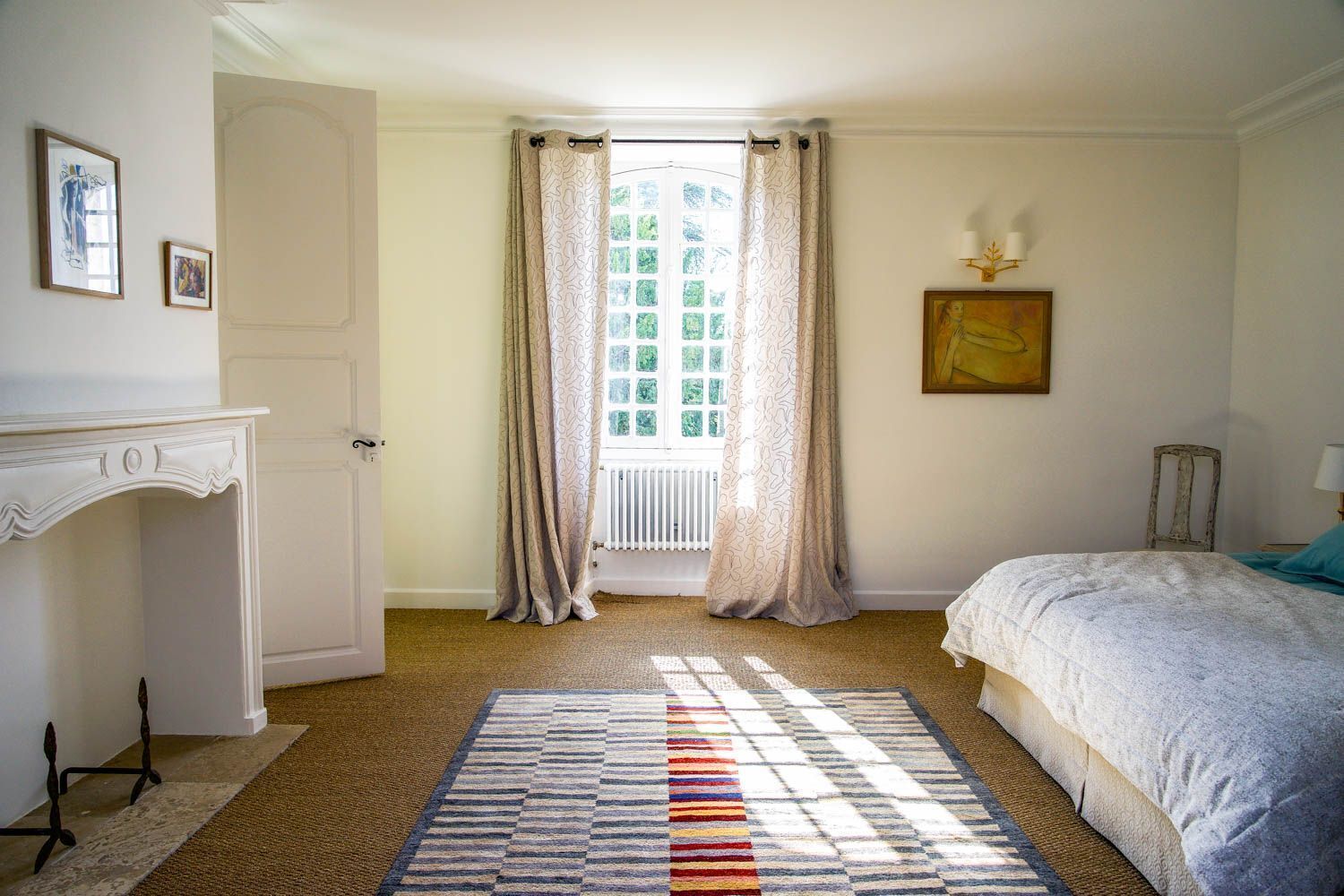 A bedroom with a bed, a radiator, a window with curtains, a fireplace, and a rug.