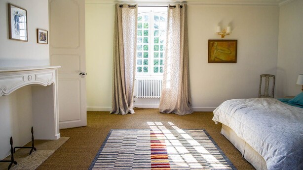 A bedroom with a bed, a radiator, a window with curtains, a fireplace, and a rug.