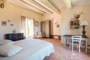 A bedroom with a bed, a desk, a chair, a dresser, and a shelf with books and a vase.