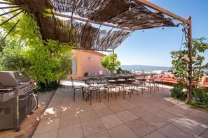 An outdoor patio with a grill, dining table, and chairs, overlooking a scenic view.