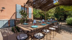 An outdoor dining area with a long wooden table, metal chairs, and a thatched roof. - Mas Du Chateau - Six Bedroom Villa, Sleeps 14 (Trets)