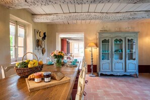 Une cuisine rustique avec une table en bois, un panier de fruits, un vase rempli de fleurs et un buffet aux portes vitrées.
