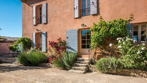 A rustic building with a stone staircase leading to a wooden door, surrounded by lush greenery and flowering plants. - Mas Du Chateau - Six Bedroom Villa, Sleeps 14 (Trets)