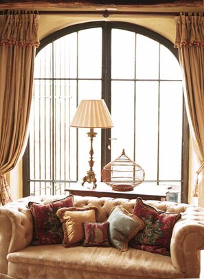 Une pièce chaleureuse avec une grande fenêtre en arc de cercle, un canapé moelleux agrémenté de nombreux coussins, une lampe de table classique et une cage à oiseaux décorative.