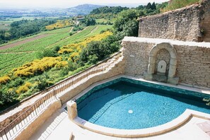 Ein Schwimmbecken mit Steinmauer und Bogen, umgeben von einer Steinterrasse und einem Metallgeländer.