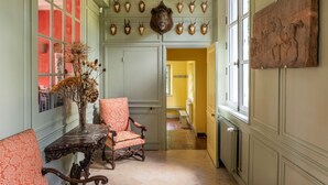 A hallway with a table and chairs, a vase with dried flowers, and a wall with mounted animal heads and a sculpture. - Chateau Falaises - Nine Bedroom Castle, Sleeps 15 (Ingouville)