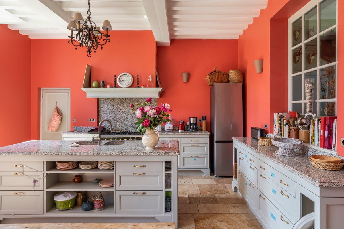 Una cocina con una isla grande, armarios blancos y una pared de acento roja.
