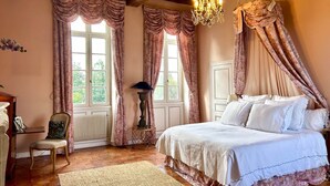Une chambre à coucher avec un grand lit, un lustre et deux fenêtres avec des rideaux.