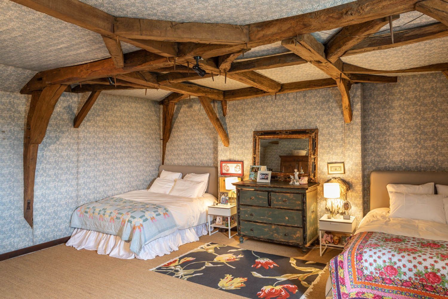 Quarto com cama grande, penteadeira, mesa de cabeceira, espelho e vigas de madeira aparente no teto.