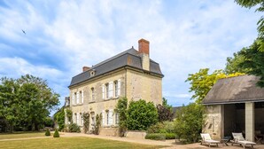 Un grand bâtiment en pierre doté d’une piscine, entouré de verdure et d’une pelouse bien entretenue.
