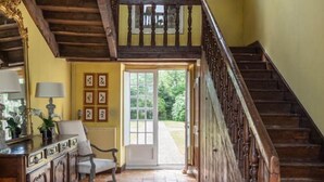 Un hall d’entrée spacieux, doté d’un escalier en bois, d’un plafond haut et offrant une vue sur l’extérieur grâce à une porte vitrée.