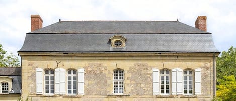 A large, historic building with a symmetrical facade, multiple windows with shutters, and a central entrance.
