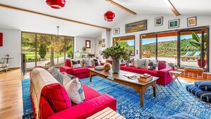 A spacious living room with a red sofa set, a coffee table, and a large window offering a view of a garden and hills.