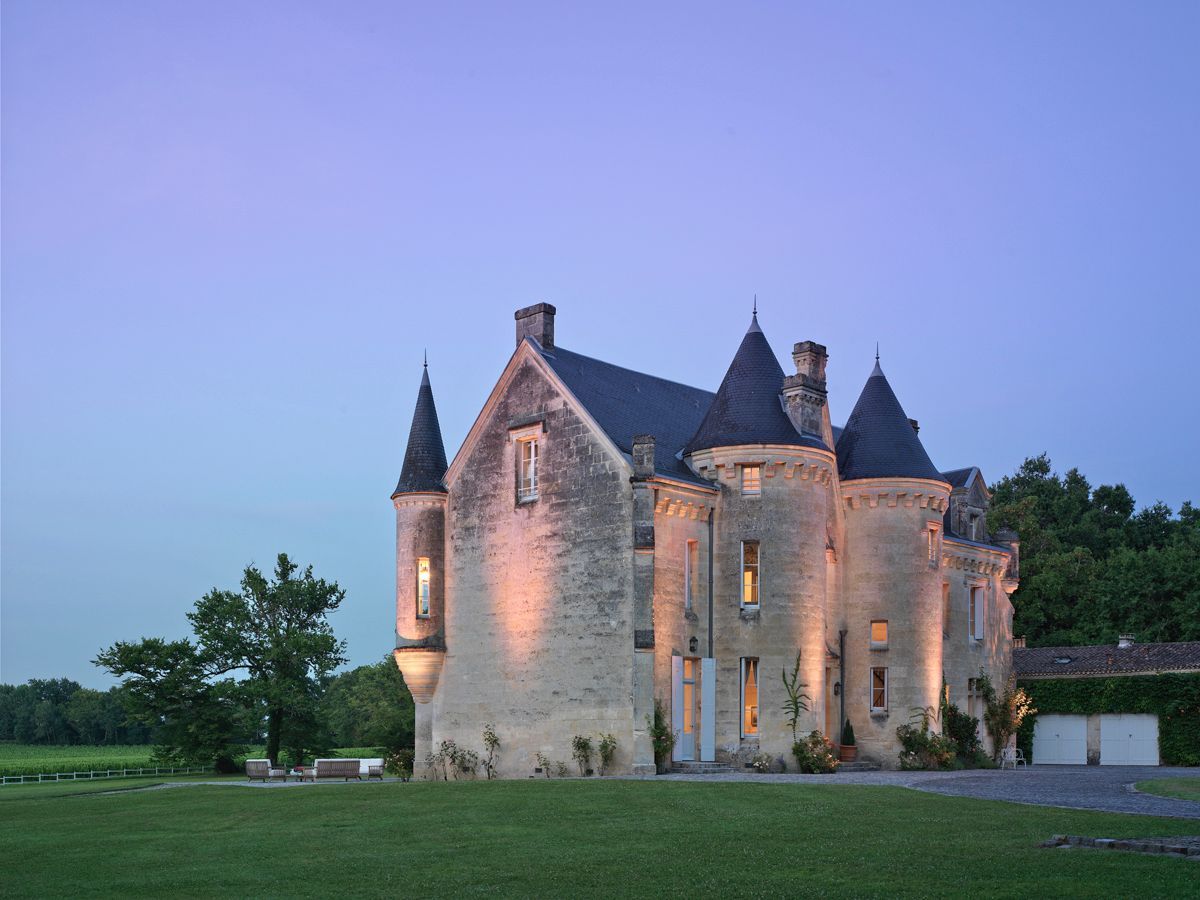 A large, historic stone castle with multiple towers and a well-maintained lawn.