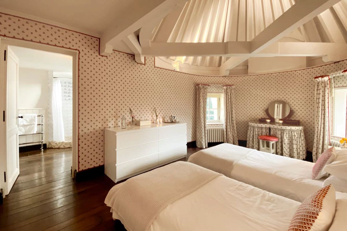 A bedroom with two beds, a dresser, a vanity with a mirror, and a window with curtains.