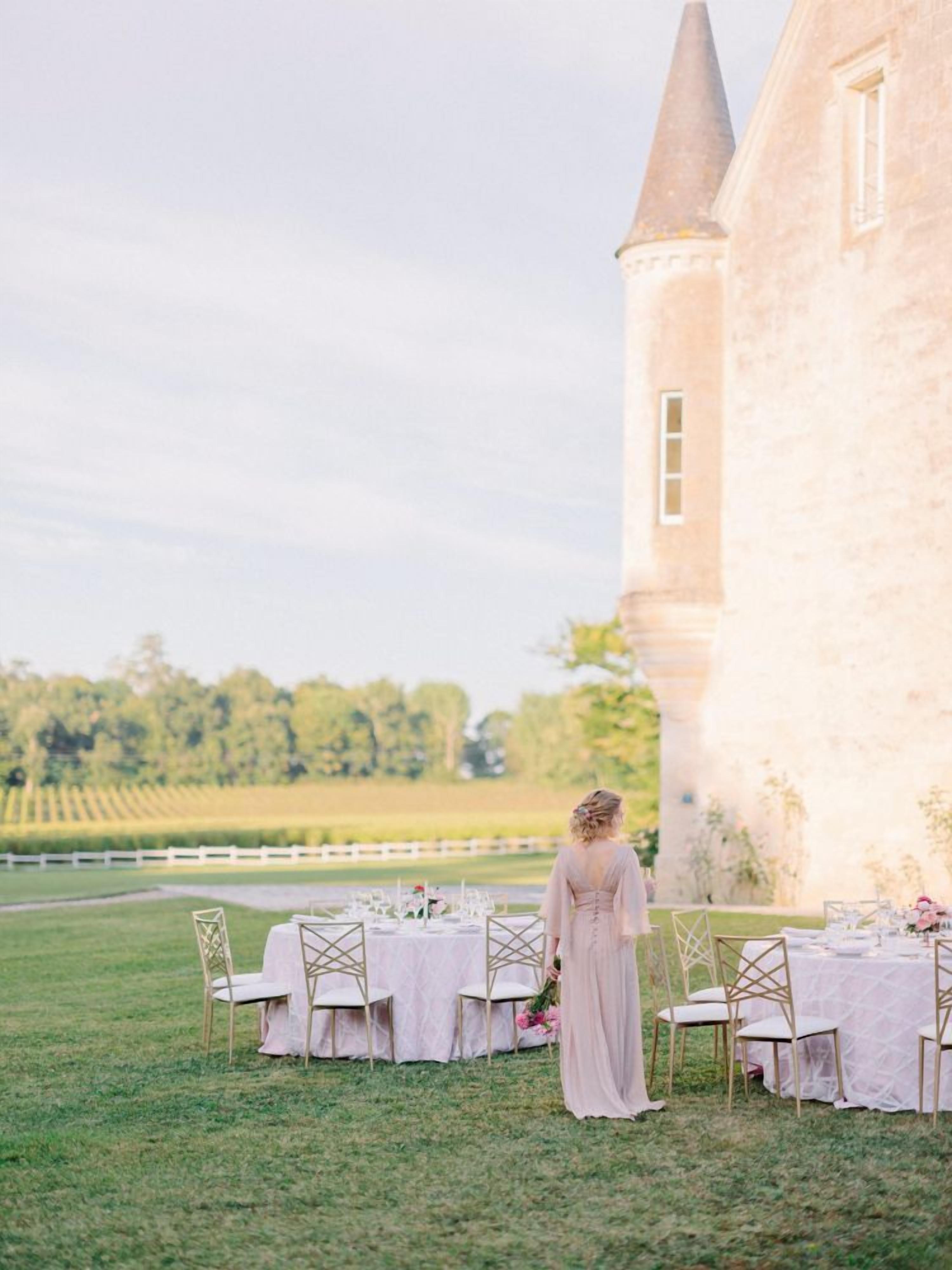 Une cérémonie de mariage en plein air, avec une table et des chaises disposées sur une pelouse, un bâtiment en arrière-plan et une personne portant une robe.