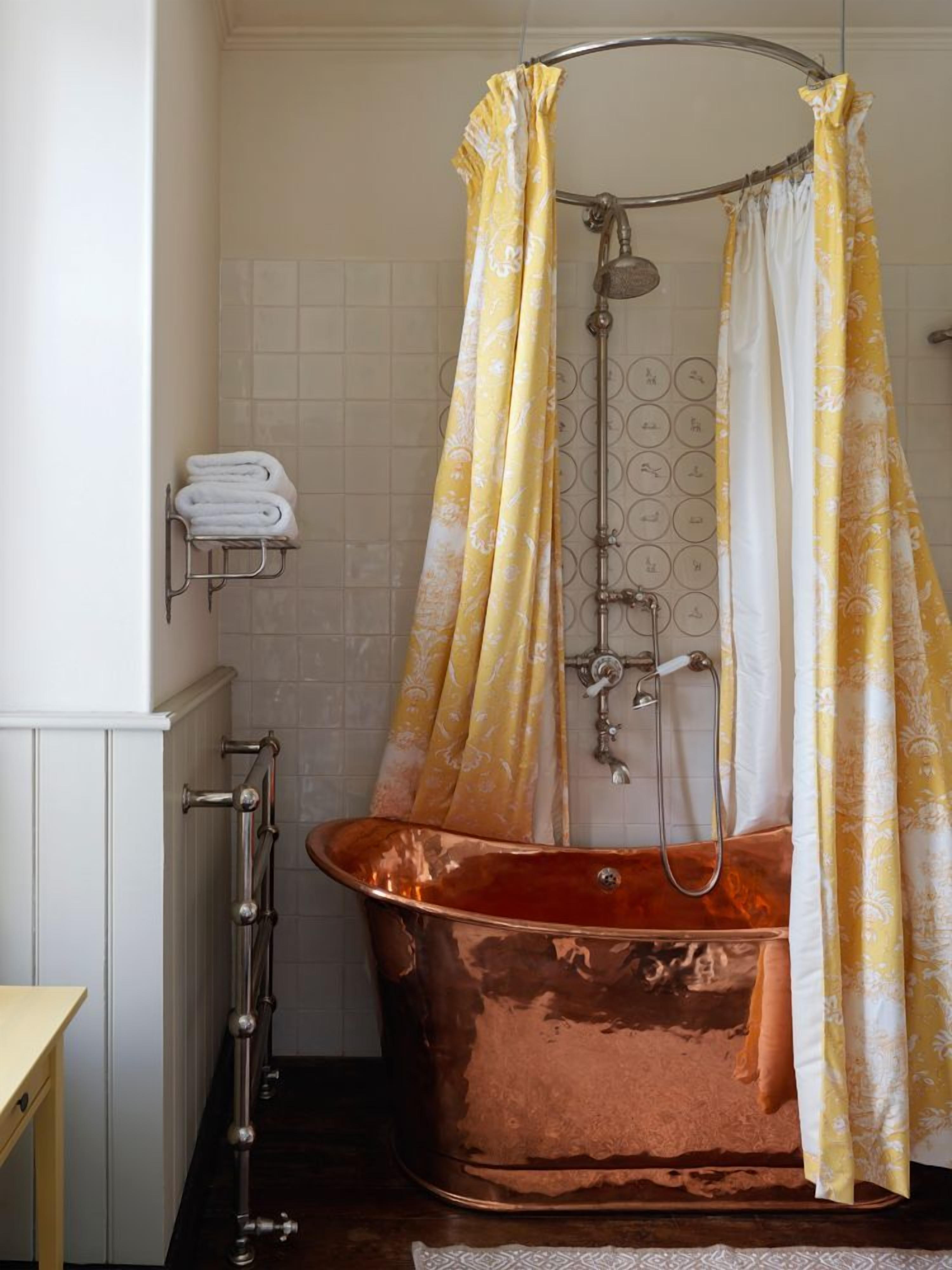 Une salle de bain avec une baignoire sur pieds en cuivre, une douche avec un rideau de douche à motifs floraux jaunes et un porte-serviettes avec des serviettes pliées.