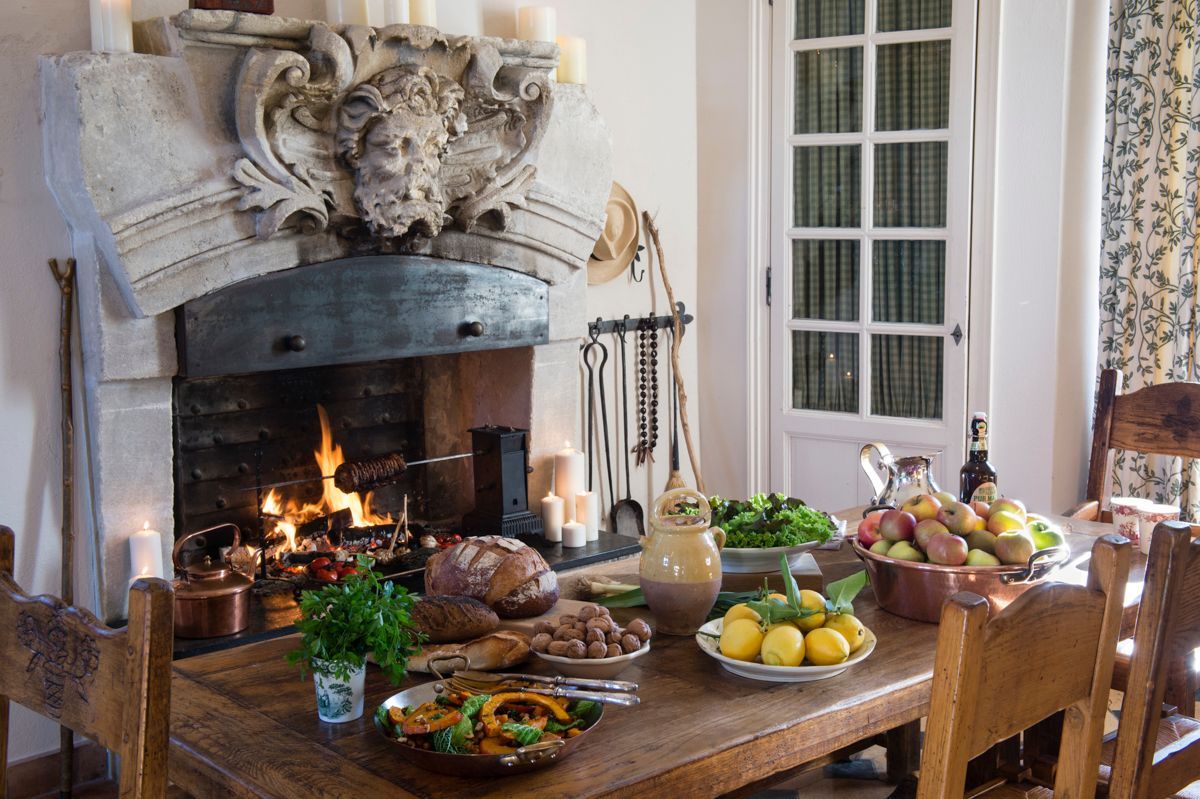 Een kamer met een open haard, een eettafel gedekt met eten en drinken, en een raam met gordijnen.
