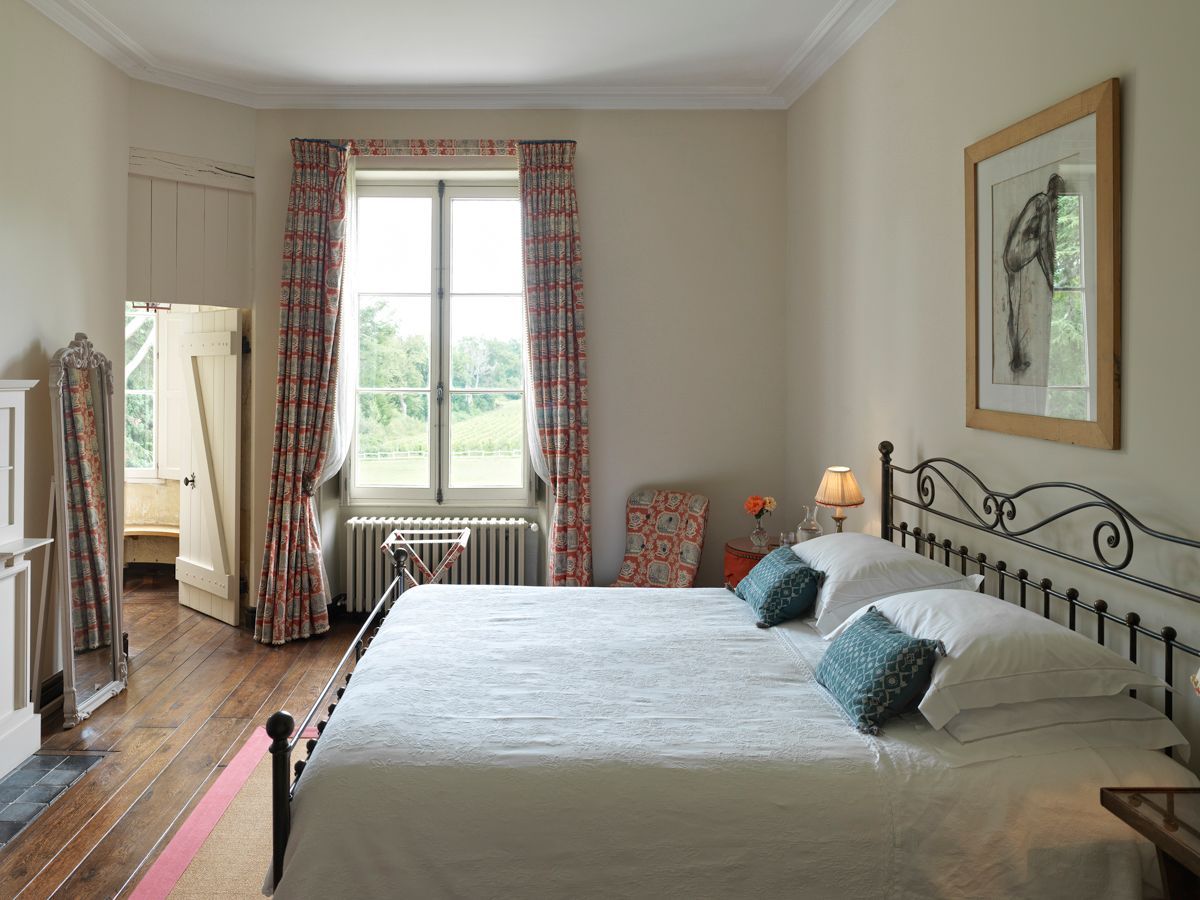 Une chambre avec un grand lit, un radiateur, une fenêtre avec des rideaux, une lampe et un tableau encadré au mur.