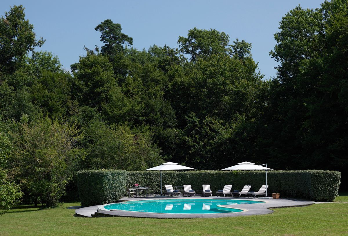 Une piscine entourée d’une haie et d’arbres, avec des chaises longues et des parasols.