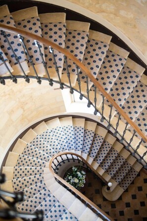 A spiral staircase with a patterned carpet and a central floral arrangement.
