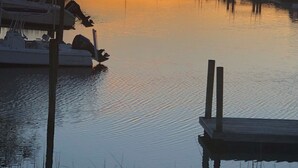 A marina at sunset with boats docked, calm water, and houses in the background. - Waterfront Canal Home - Private Boat Dock, Elevator & Short Walk to Beach Access (Holden Beach)