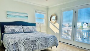 A bedroom with a bed, a nightstand, a wall-mounted mirror, and a window with blinds. - Waterfront Canal Home - Private Boat Dock, Elevator & Short Walk to Beach Access (Holden Beach)