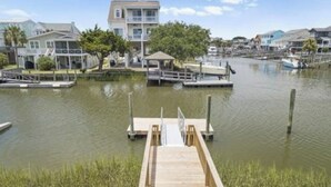 A wooden dock leading to a marina with boats, a small pavilion, and houses in the background. - Waterfront Canal Home - Private Boat Dock, Elevator & Short Walk to Beach Access (Holden Beach)